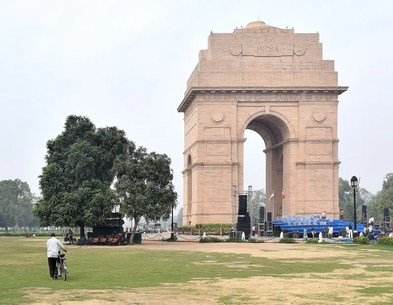 The sandstone arch of India Gate behind a lawn and a large tree