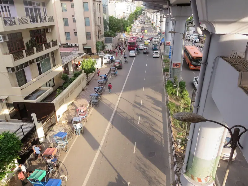A street seen from above with rickshaws, parked cars and a bus between shops and houses